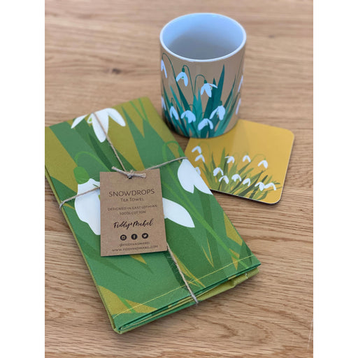 Snowdrop printed teatowel, mug and coaster placed on a wooden kitchen worktop