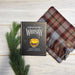 Field Guide Whisky book laid on the Outlander Tartan Stole next to some green shrubbery
