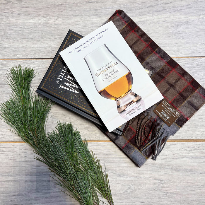 Whiskypedia Guide book laid on the Oulander Tartan Stole next to some shrubbery 