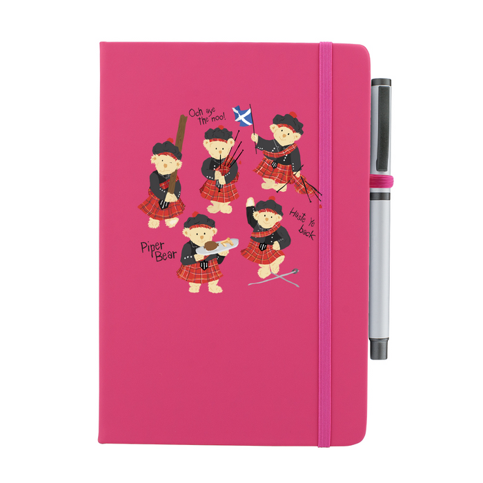 A beautiful designed pink notebook featuring a vibrant illustration of dancing piper bears in red and black, playing bagpipes joyfully. A pink strap closes over the right hand side with a matching pen.