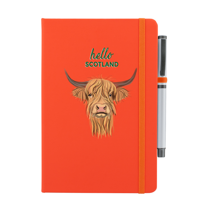 Soft Touch orange notebook featuring a Highland Cow and the test reads 'hello SCOTLAND'. An orange strap closes over the right hand side with a matching pen.