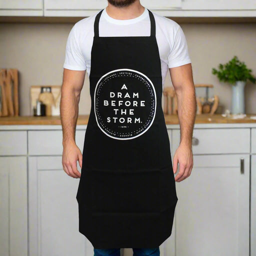 dram before the storm apron shown on model wearing tshirt and soft focus kitchen in background