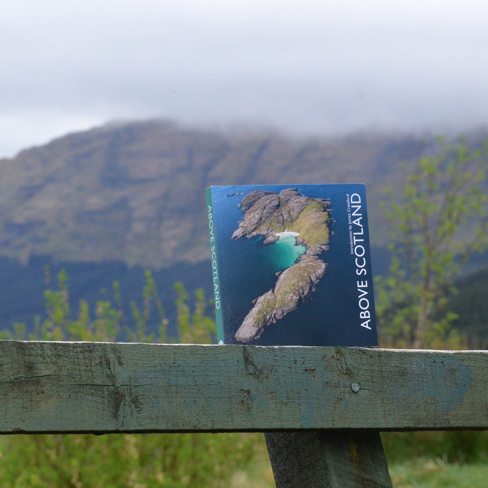 book shown in landscape propped on wooden fence with misty topped scottish mountains in backdrop