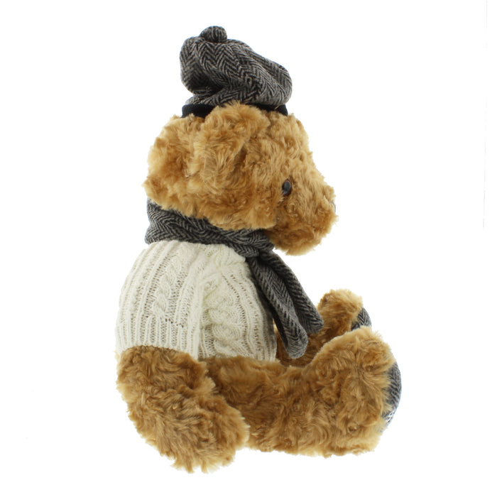 Side view of a soft brown teddy bear wearing an Arran jumper, tweed hat and scarf. 