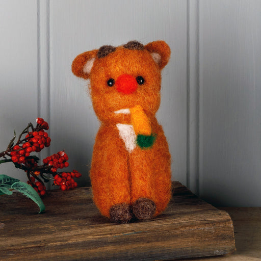 Felt baby Rudolph made and sat on a piece of wood next to some festive berries 