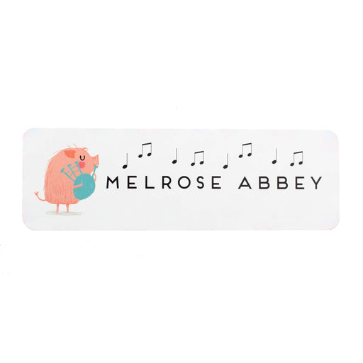 Slim white bookmark features the word MELROSE ABBEY and has a small pink pig playing the bagpipes