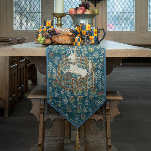 captive unicorn tapestry table runner shown drapped on end of table at castle with heraldic tableware and medieval banquet set on table