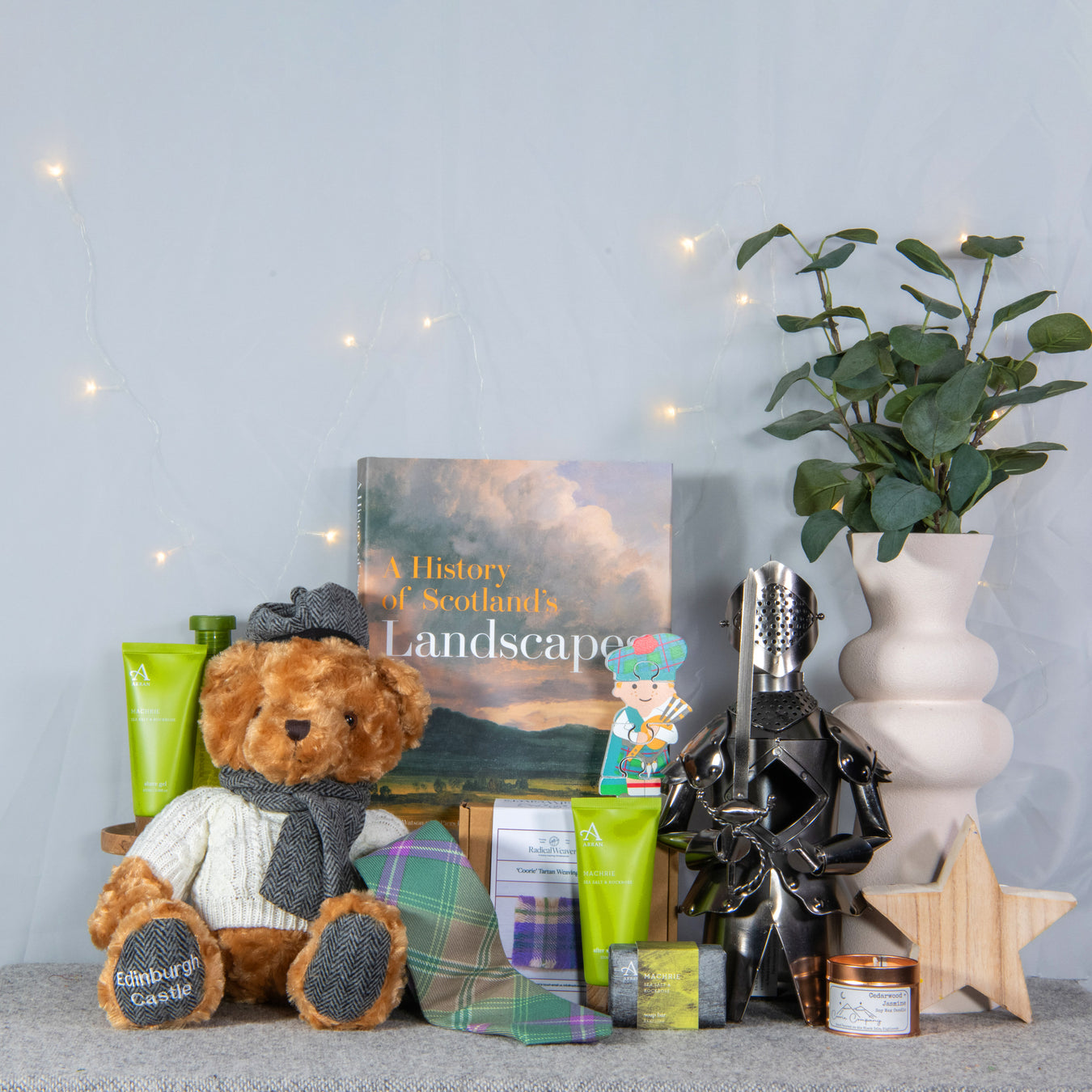 group of shop gifts shown together with teddy, tie, knight bottle holder and others sitting in front of wall with fairy lights