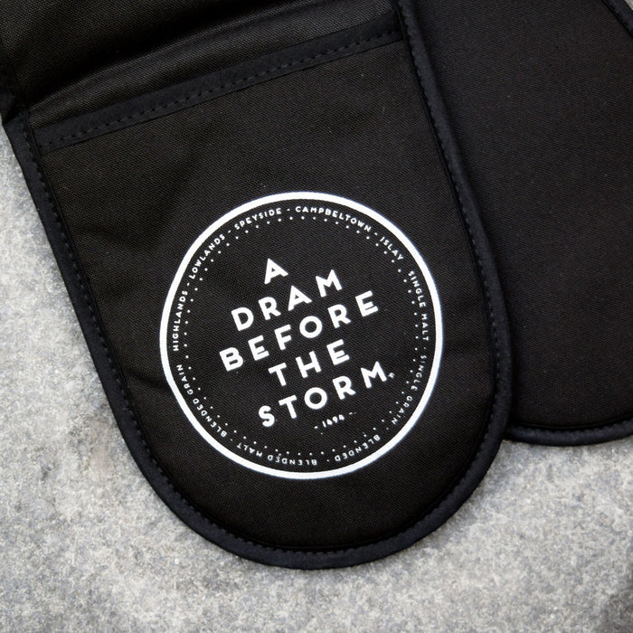 black cotton oven gloves with dram before the storm printed in white text on side