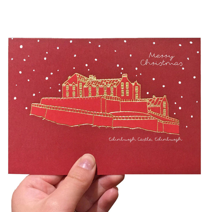 Red Christmas card with Edinburgh Castle illustration in gold foil with words merry christmas and edinburgh castle, edinburgh. card is held by a hand in foreground - Image