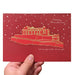 Red Christmas card with Edinburgh Castle illustration in gold foil with words merry christmas and edinburgh castle, edinburgh. card is held by a hand in foreground - Image
