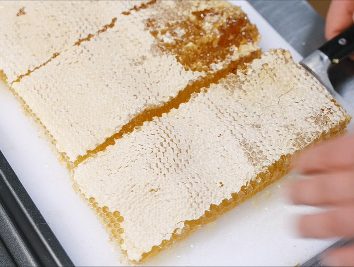 close up shot of 3 layers of honeycomb lying flat on surface with waxy tops and person placing knife underneath to lift a slice