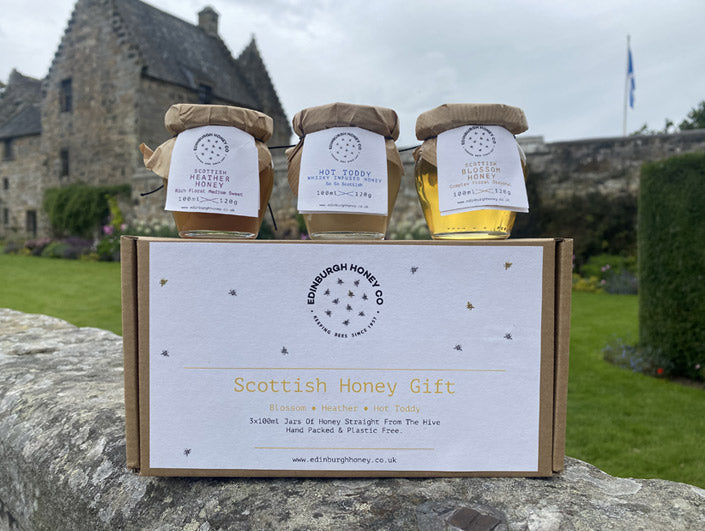 3 jars of honey sitting on gift box on stone wall in front of aberdour castle in gardens