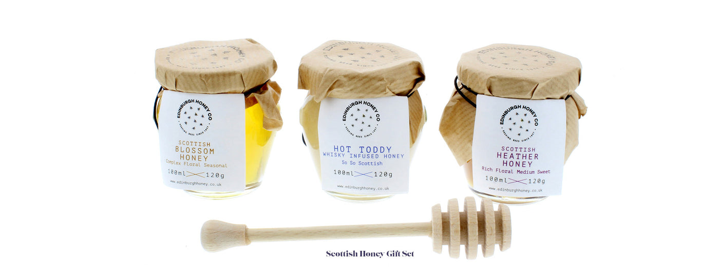 3 jars of scottish honey flavours sitting side by side with wooden honey dripper in front of them and words scottish honey gift set