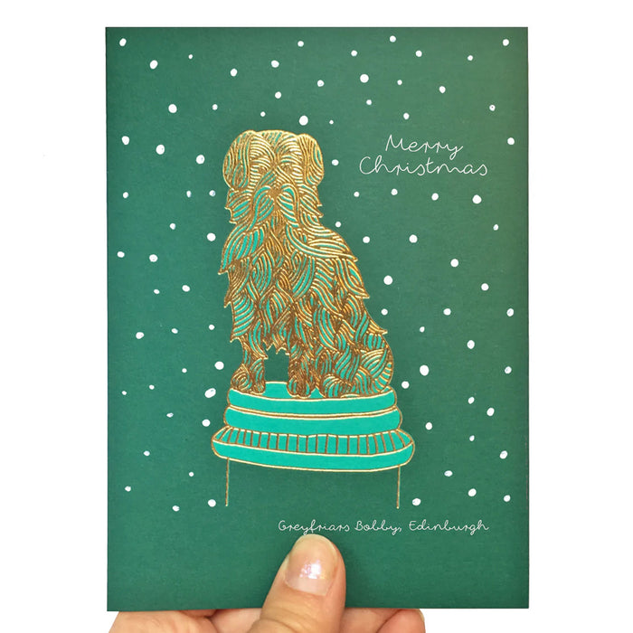 green christmas card with gold fold embossed greyfriars booby dog illustration, round snowflakes and the words merry christmas greyfriars bobby edinburgh in handwritten script - Image