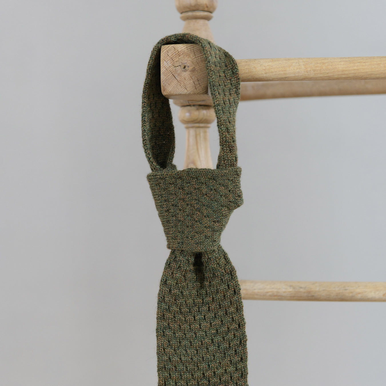 A green coloured knitted tie hangs on a wooden clothes horse. 