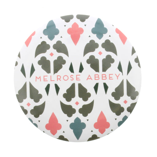Small round mirror features the words Melrose Abbey surrounded by a colourful window inspired print 