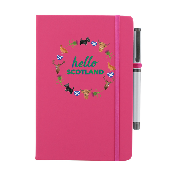 A beautiful designed pink notebook with the words 'Hello Scotland' in green,  featuring elements of Scottish culture and scenery. A pink strap closes over the right hand side with a matching pen.