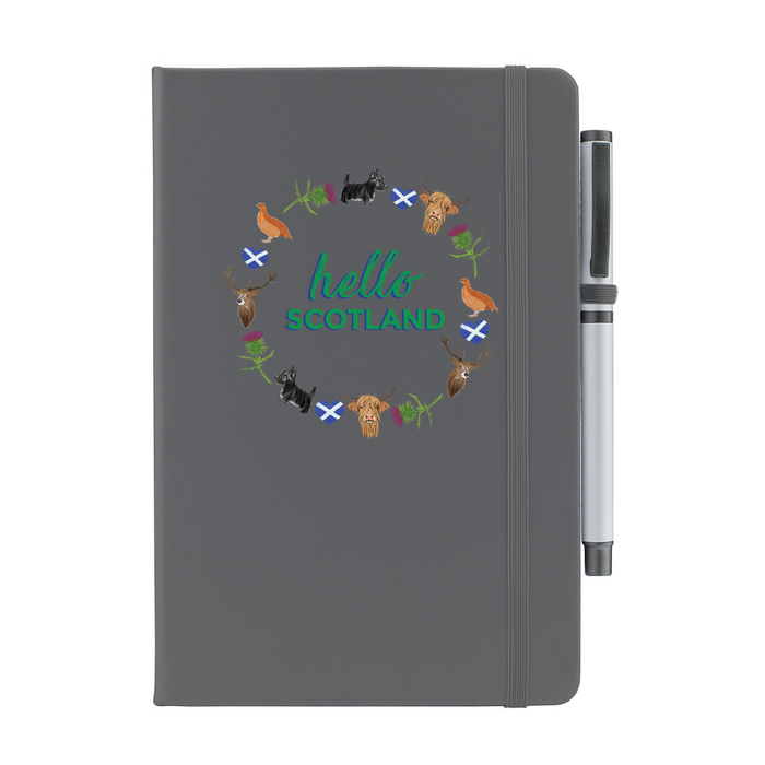 Grey notepad with pen features a circular prints of Scottish Icons including the St Andrews Flag in a loveheart shape, a pheasant and a deer. A matching strap closes on the right hand side.