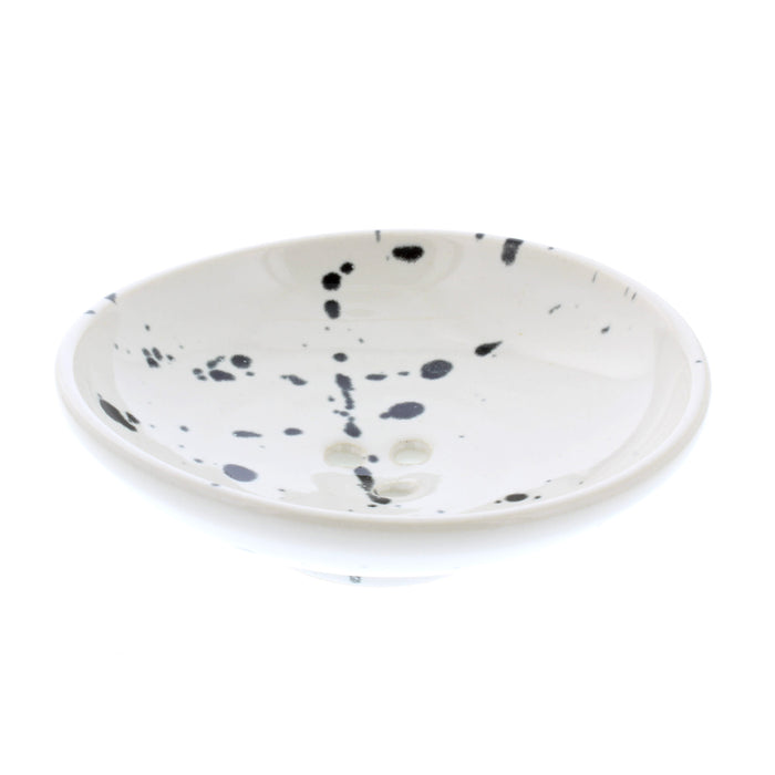 light coloured circular soap dish with a black paint splash effect pattern