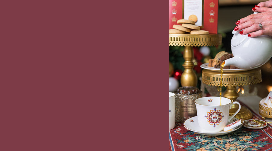 Tea cup and saucer on a patterned tablecloth with a teapot and shortbread in the background. - Image