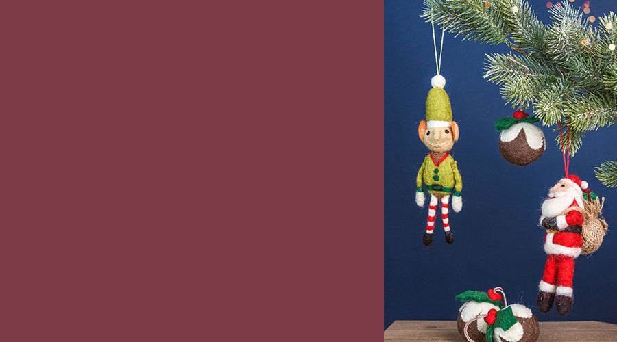 Christmas decorations including an elf and Santa Claus ornaments on a tree against a blue wall. - Image