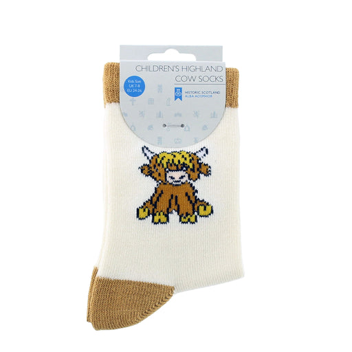 A pair of children's Highland cow socks in cream and tan, featuring a Highland cow graphic on the front, packaged on a white cardboard hanger. - Image