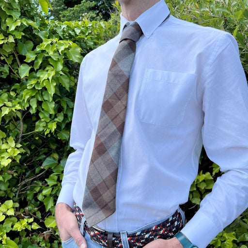 Person stands in front of some greenery wearing a white shirt and the outlander tartan tie. 