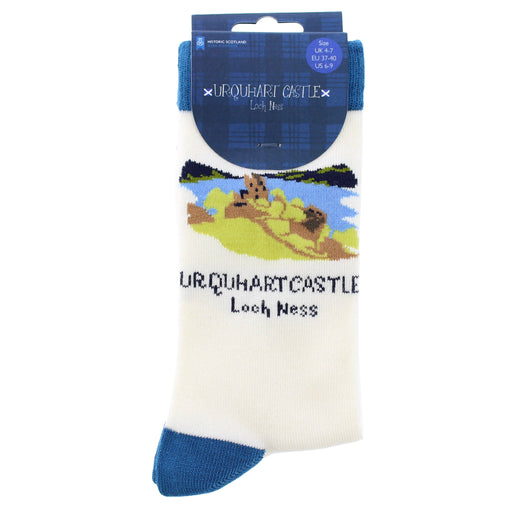 A pair of white crew socks with blue heels and toes, featuring a printed graphic of Urquhart Castle and Loch Ness, packaged on a blue header card. - Image