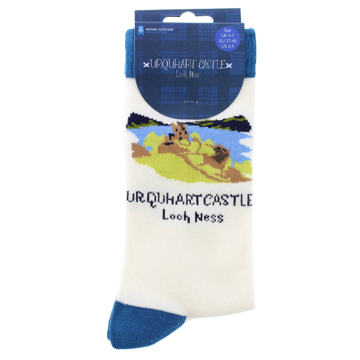 A pair of white crew socks with blue heels and toes, featuring a printed graphic of Urquhart Castle and Loch Ness, packaged on a blue header card. - Image