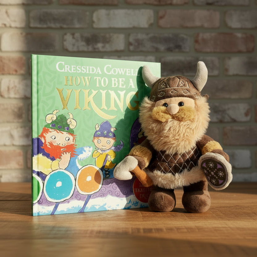 Plush toy Viking figure next to a book titled 'How to Be a Viking' by Cressida Cowell. - Image