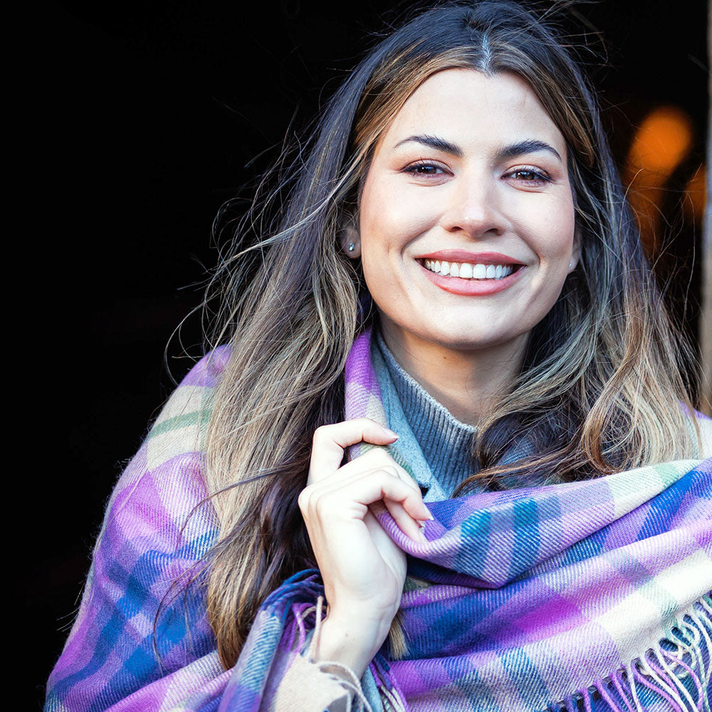 Woman wrapped in the Coorie Throw standing against a stone wall. - Image