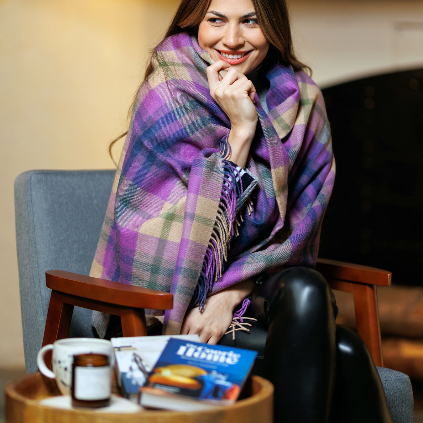 Woman sitting in a chair with a purple plaid scarf, holding a book and a cup of coffee. - Image