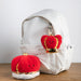 Two red plush toys with gold crowns attached to a white backpack on a wooden surface. - Image