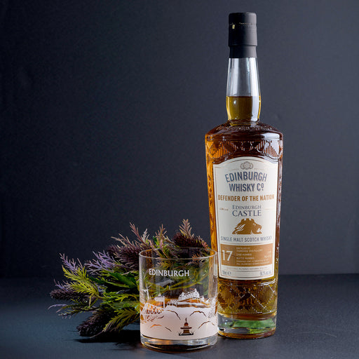 Bottle of Whisky, a glass and some dried thistles against a dark backdrop. - Image