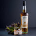Bottle of Whisky, a glass and some dried thistles against a dark backdrop. - Image
