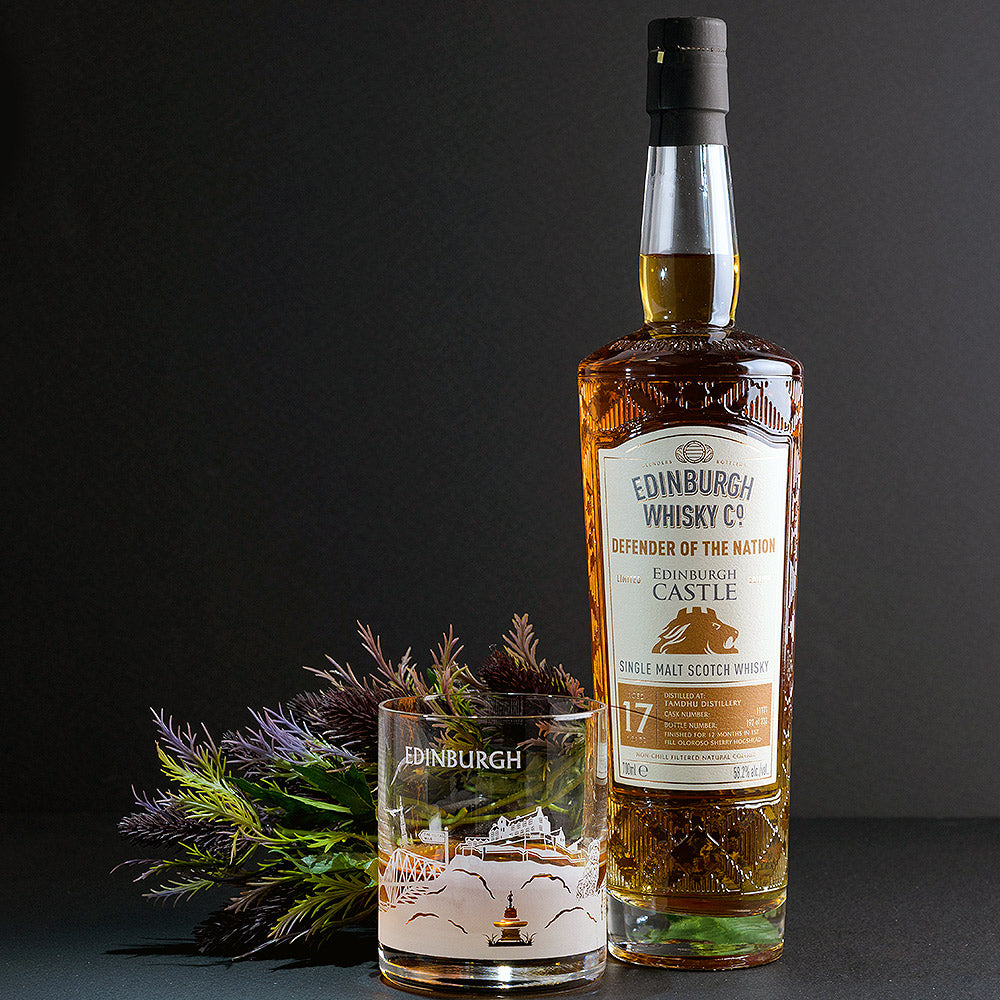 Bottle of Whisky, a glass and some dried thistles against a dark backdrop. - Image