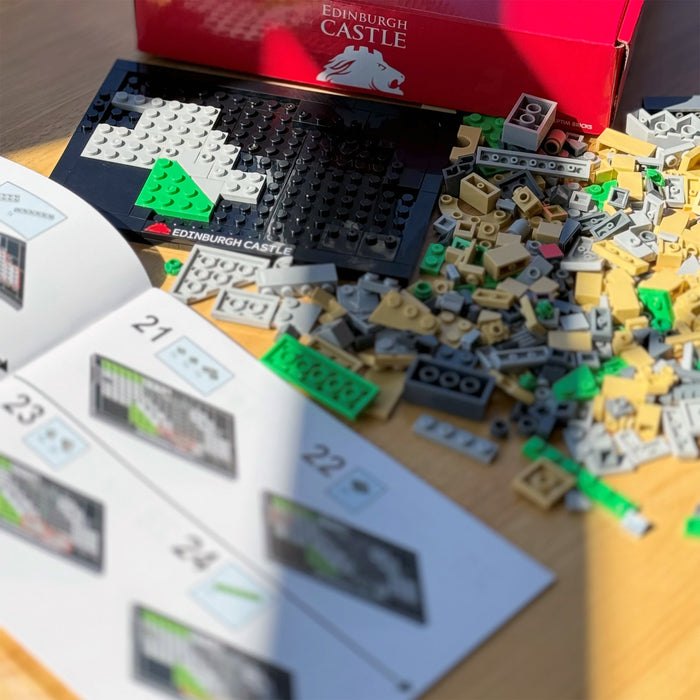 Brick pieces and building instructions on a table with Edinburgh Castle branding. - Image