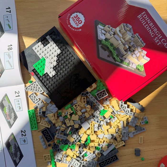 Scattered brick pieces with a red box labeled 'Edinburgh Castle Building Set' on a wooden surface. - Image