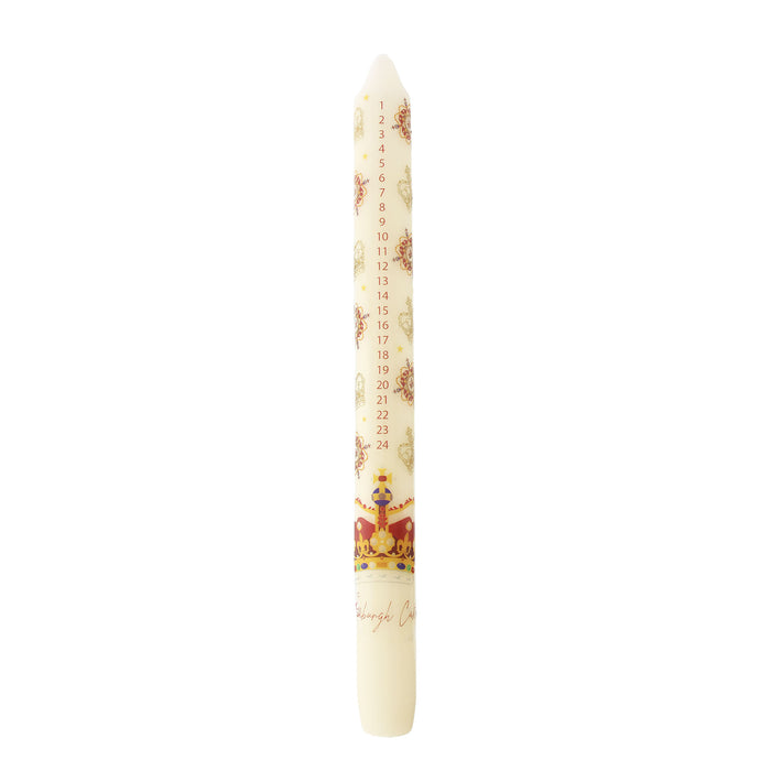 A Christmas advent candle with a cream-colored body, decorated with a printed calendar of the twelve days, small illustrations, and the Crown Jewels at the bottom. - Image
