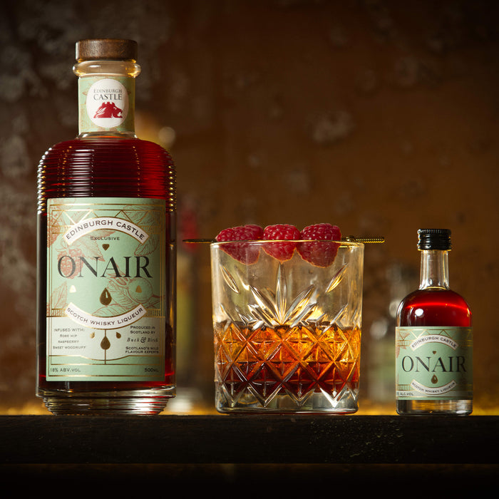 Whisky Liqueur bottles with green labels sit either side of a drink with raspberries.  - Image