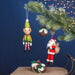 Christmas ornaments including a elf, pudding, and Santa Claus hanging from a tree branch against a dark blue background. - Image