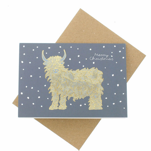 Greeting card with gold highland cow illustration on a blue background with white dots, featuring 'Merry Christmas' text, on a brown envelope. - Image