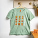 Mint green kids t-shirt with highland cow print hanging on a peg against a white wall - Image