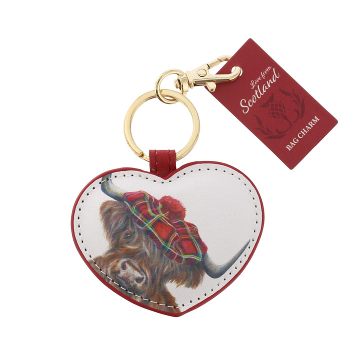 Heart-shaped bag charm featuring a Highland cow illustration wearing a red tartan kilt, attached to a gold-tone keyring and a red 'Love from Scotland Bag Charm' tag, on a white background. - Image