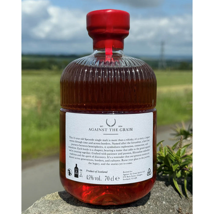 Bottle of 'Against The Grain' Hirundine whisky with a red cap against a natural landscape - Image