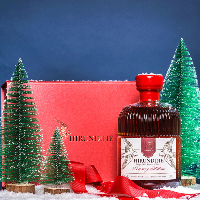 Bottle of Hirundine whisky with a red box and Christmas trees in the background - Image