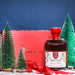 Bottle of Hirundine whisky with a red box and Christmas trees in the background - Image