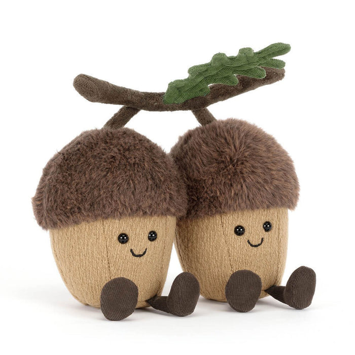 Two plush acorn toys with brown faux-fur caps, beige bodies, embroidered smiling faces, and small brown feet, attached to a brown branch with a green leaf on a white background. - Image