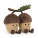 Two plush acorn toys with brown faux-fur caps, beige bodies, embroidered smiling faces, and small brown feet, attached to a brown branch with a green leaf on a white background. - Image